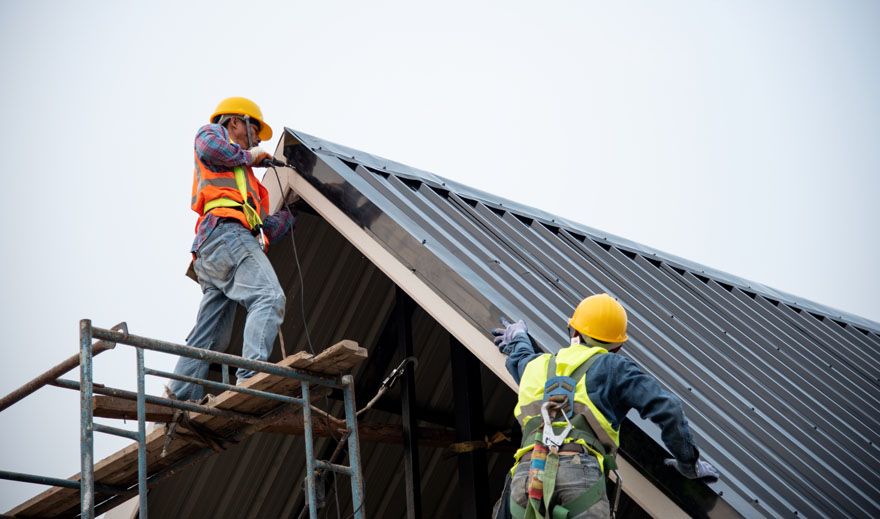 Workers installing a metal roof with safety gear.