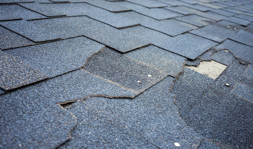 A close up image showing missing and damaged shingles on a roof that need repaired