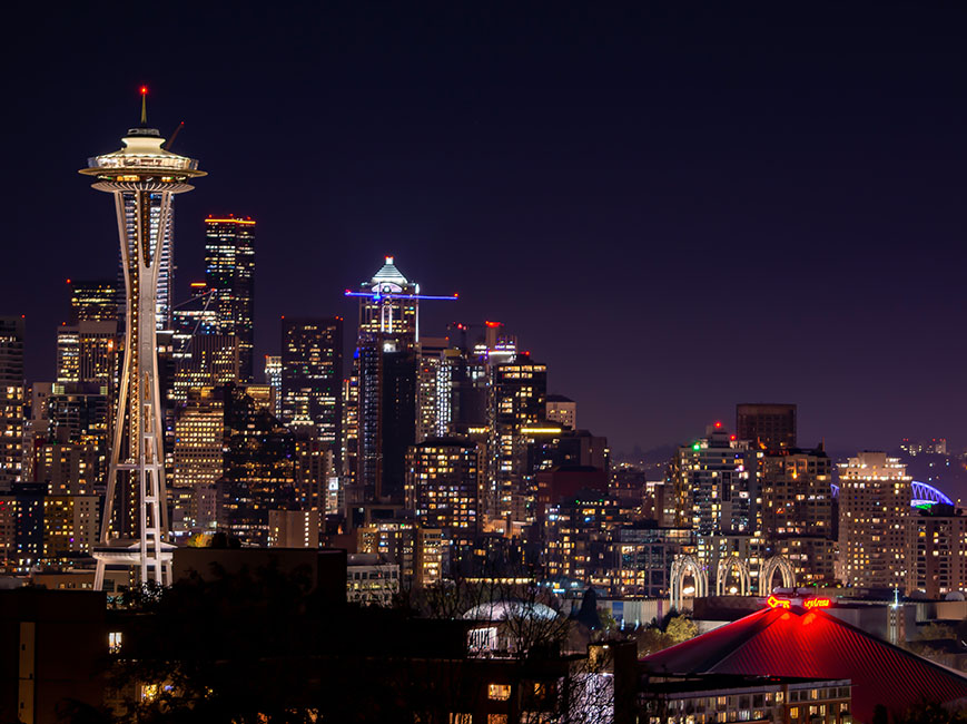 Nighttime view of Seattle featuring the illuminated Space Needle prominently against a dark cityscape.